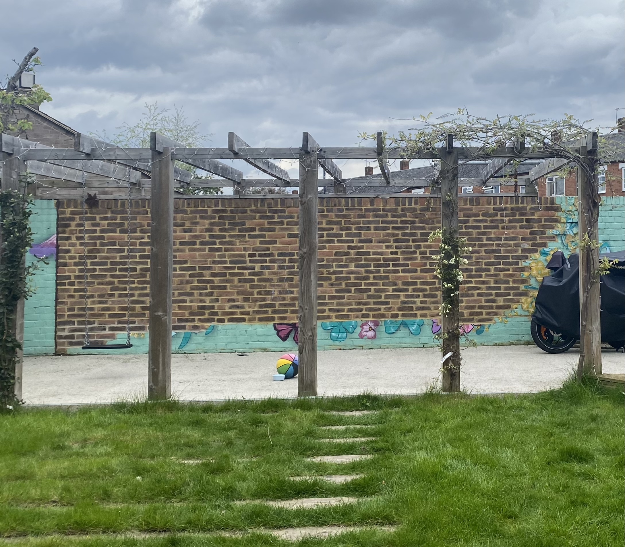 Wisteria, roses and a bluebird mural painted around a garden pergola in London